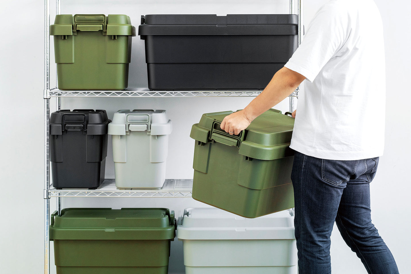 A man putting a green home storage box on the well organised shelf that full of other boxes