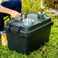 A man sitting on the grass is using a black camping storage box as a table for his camping gears